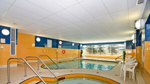 Una piscina interior con paredes de azulejos, una silla de socorrista y una ventana con vistas a árboles.
