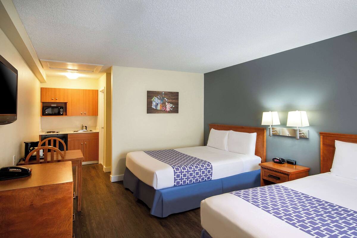 Une chambre d’hôtel avec deux lits, un bureau, une chaise, un four à micro-ondes et un petit coin cuisine.
