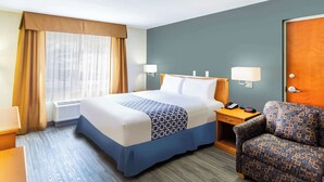 Una habitación de hotel con cama, mesita de noche, lámpara, silla y ventana con cortinas.