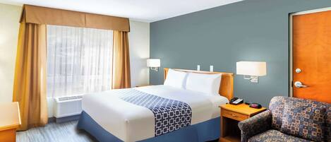 A hotel room with a bed, bedside table, lamp, chair, and a window with curtains.