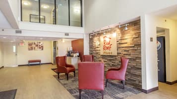 Un hall d'entrée avec une enseigne « Red Roof Plus », un espace détente avec des fauteuils, un comptoir d'accueil et un escalier menant à un étage supérieur.