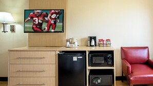 Une chambre d’hôtel équipée d’une télévision, d’une machine à café, d’un four à micro-ondes, d’un réfrigérateur, d’un fauteuil rouge et d’une commode en bois avec des tiroirs.