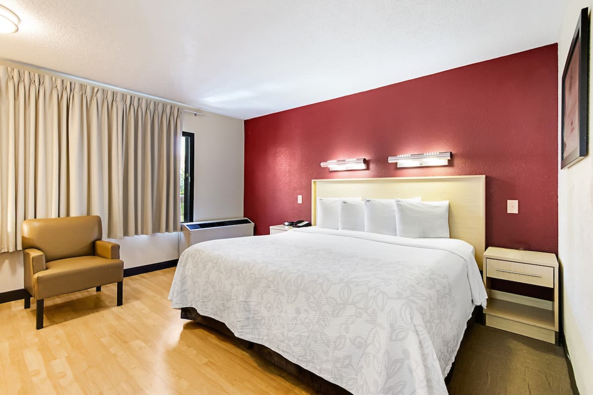 A hotel room with a bed, a chair, a nightstand, and a window with curtains.