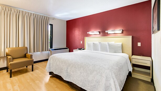Una habitación de hotel con cama, una silla, un escritorio y una ventana con cortinas.