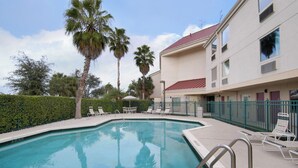 Una piscina con sillones de descanso y un edificio con tejado rojo al fondo.