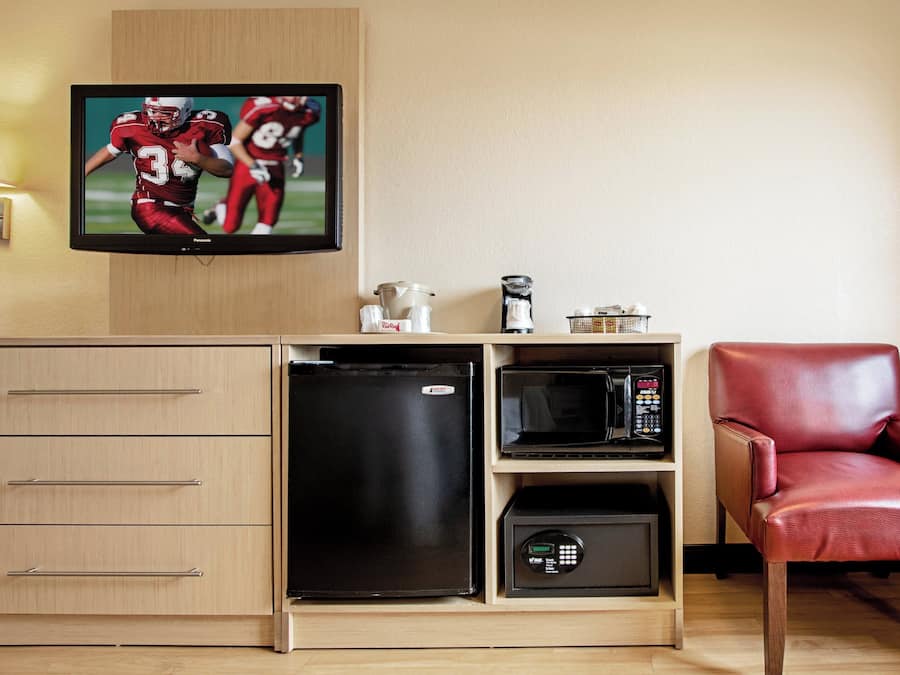 A compact kitchenette with a microwave, refrigerator, and a television displaying a sports game.