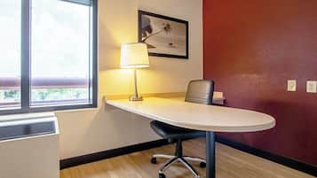 A hotel room with a desk, chair, lamp, and a window with a view.