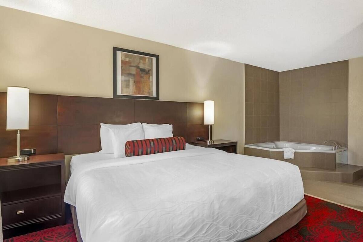 Een hotelkamer met een groot bed, twee bedlampen, een schilderij aan de muur en een aparte badkamer met een bad.