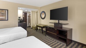 Una habitación de hotel con dos camas, un escritorio, un televisor y un espejo.