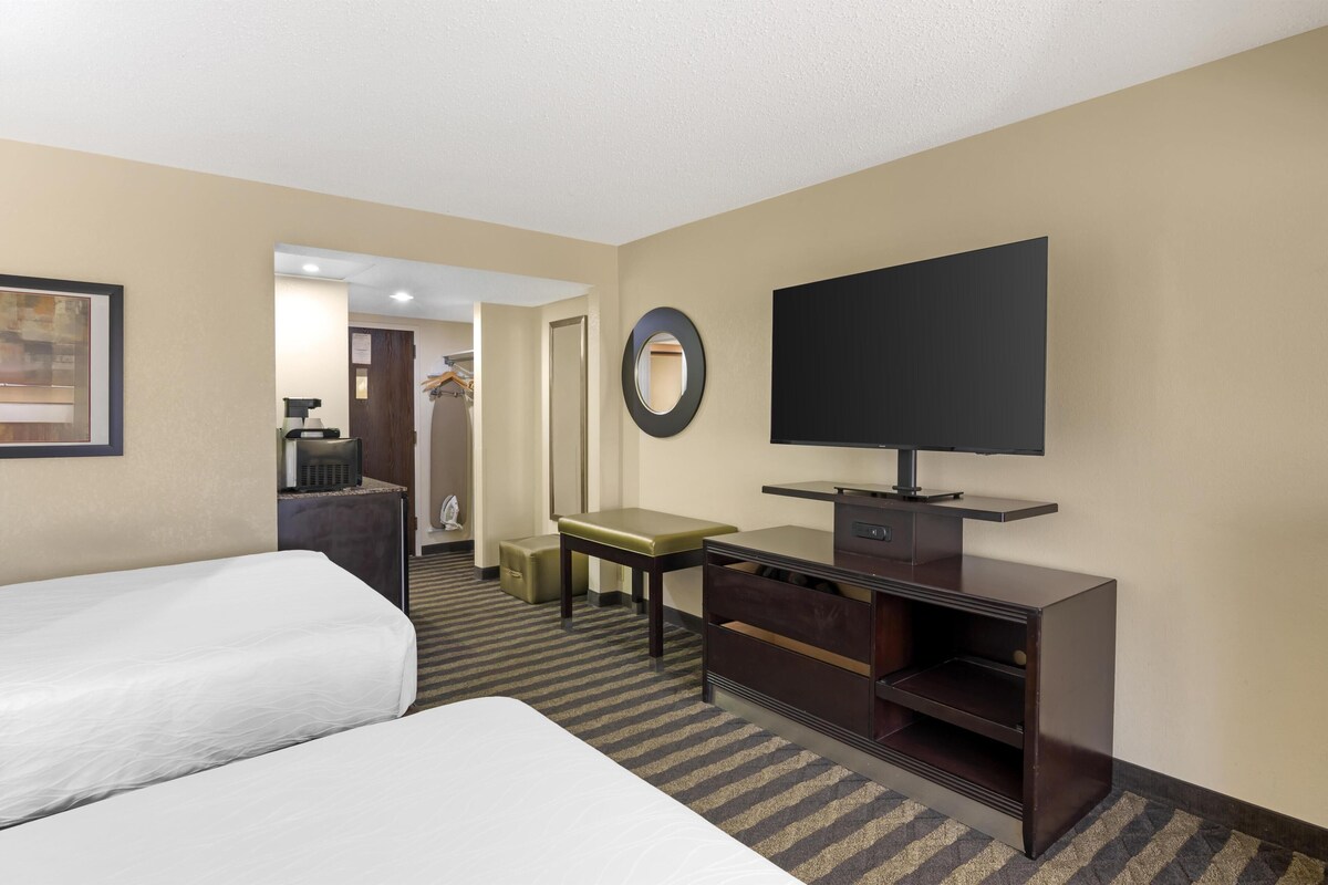 A hotel room with two beds, a desk, a television, and a mirror.