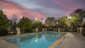 Una piscina rectangular al aire libre con un bordeado de baldosas, rodeada de sillas de descanso y una valla.