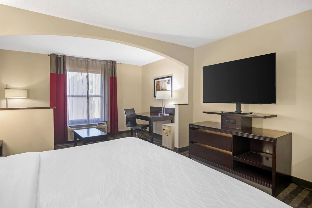 Een hotelkamer met een groot bed, een bureau met stoel, een televisie en een raam met gordijnen.