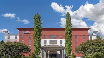 A Best Western hotel with a red and white facade, a covered entrance, and two tall trees flanking the entrance.