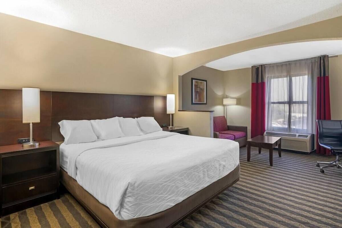 Een hotelkamer met een groot bed, nachtkastjes, een bureau, een stoel en een raam met gordijnen.