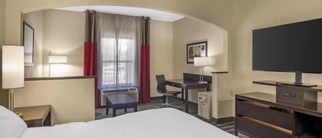 Habitación de hotel con cama, escritorio, silla, televisión y una kitchenette pequeña.