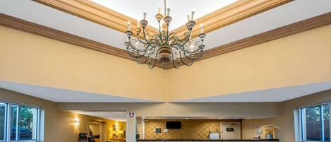 Vestíbulo de hotel con candelabro, mostrador de recepción de madera y vistas al exterior.