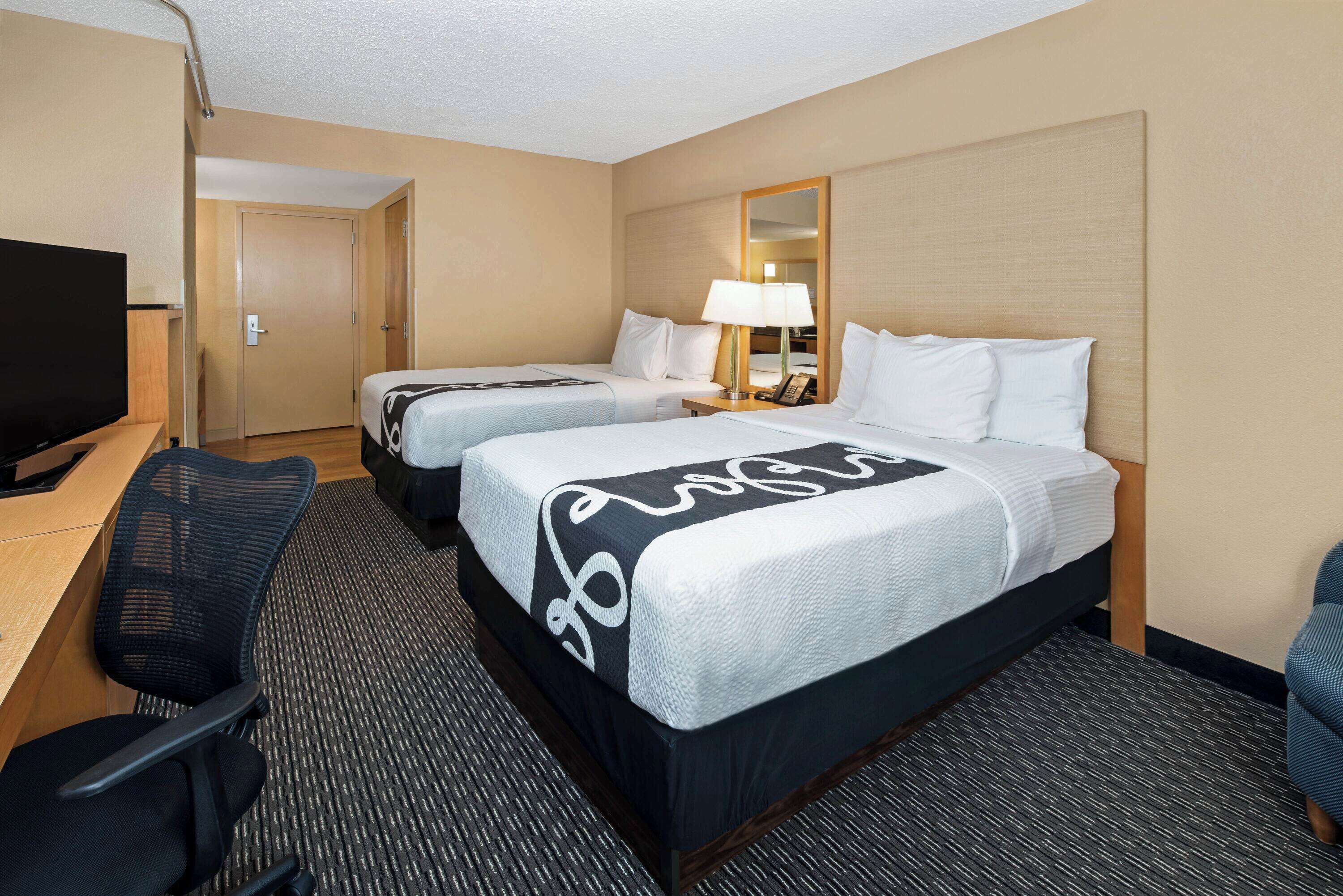 A hotel room with two beds, a desk with a chair, a television, and a mirror.