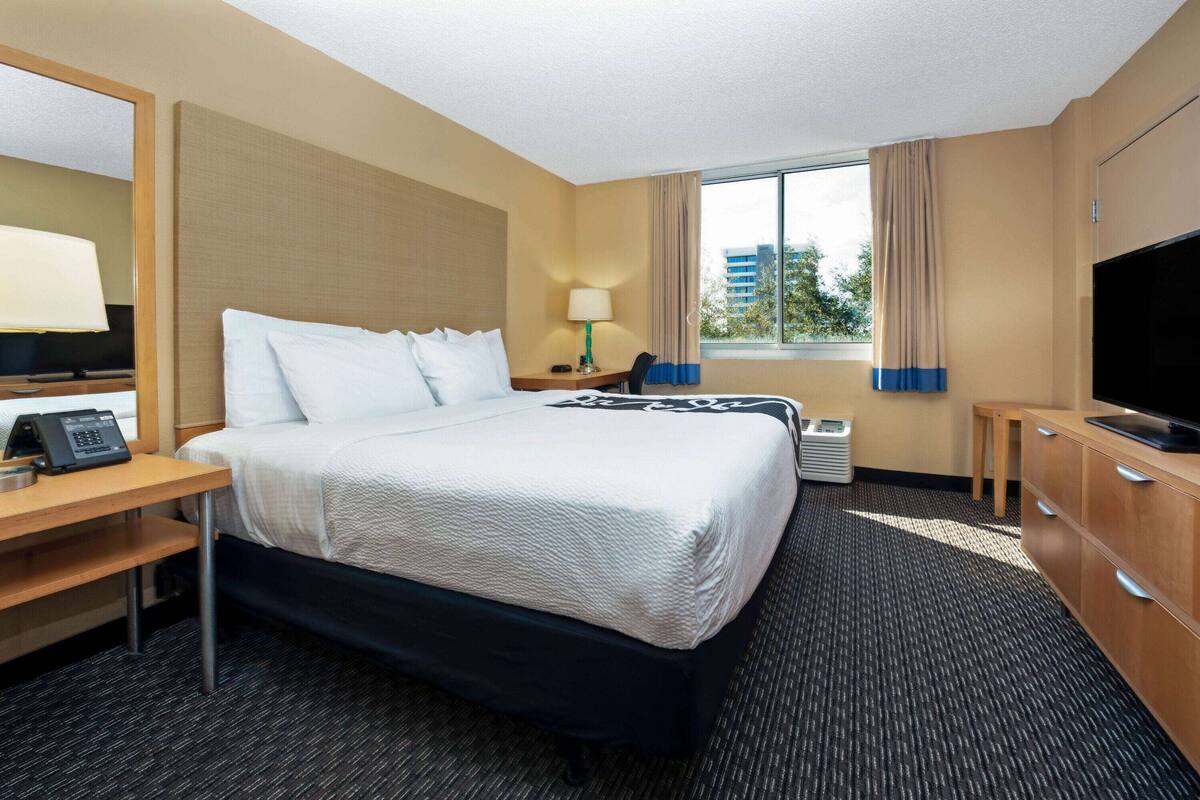 A hotel room with a bed, a desk with a telephone, a TV, and a window with curtains.