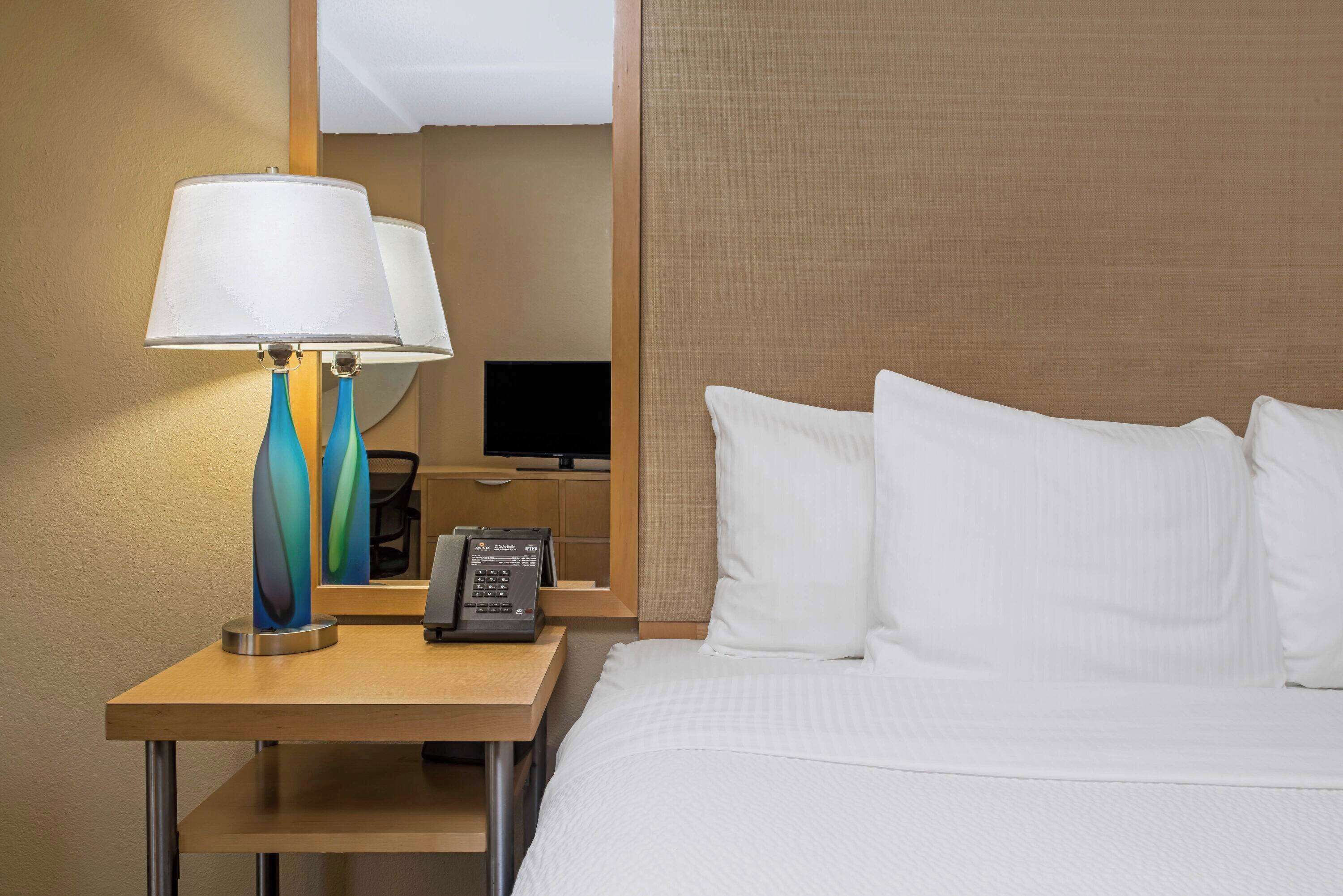 A hotel room with a bed, a nightstand with a lamp, a telephone, and a television.