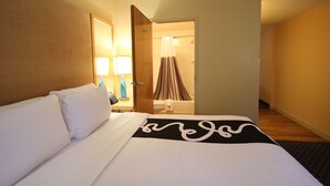 A hotel room with a bed, a nightstand with a lamp, and a bathroom visible through an open door. - La Quinta Inn & Suites by Wyndham West Palm Beach Airport (West Palm Beach)