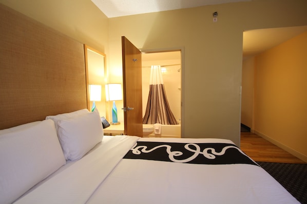 A hotel room with a bed, a nightstand with a lamp, and a bathroom visible through an open door.