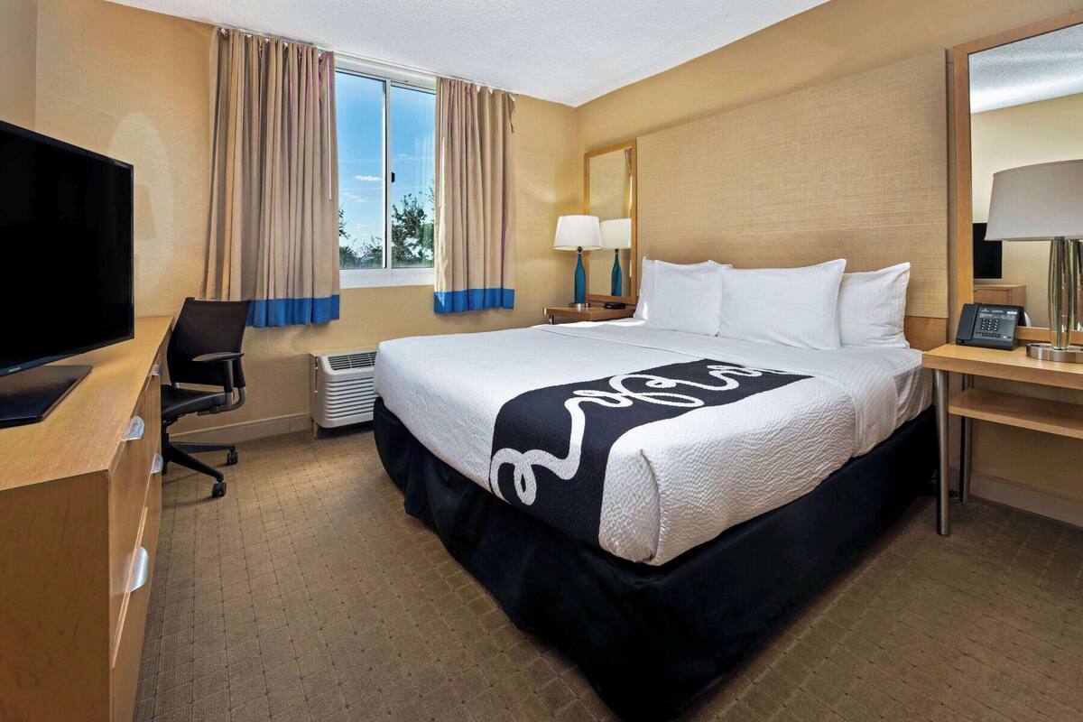 A hotel room with a bed, a desk, a television, a lamp, and a window with curtains.