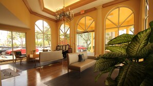 A spacious lobby with a sofa, chairs, a chandelier, large windows, and a potted plant. - La Quinta Inn & Suites by Wyndham West Palm Beach Airport (West Palm Beach)