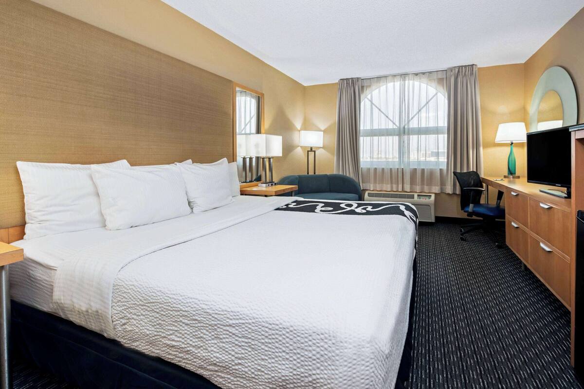 A hotel room with a large bed, two bedside tables, a desk with a chair, a television, and a window with curtains.