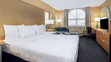 A hotel room with a large bed, two bedside tables, a desk with a chair, a television, and a window with curtains.