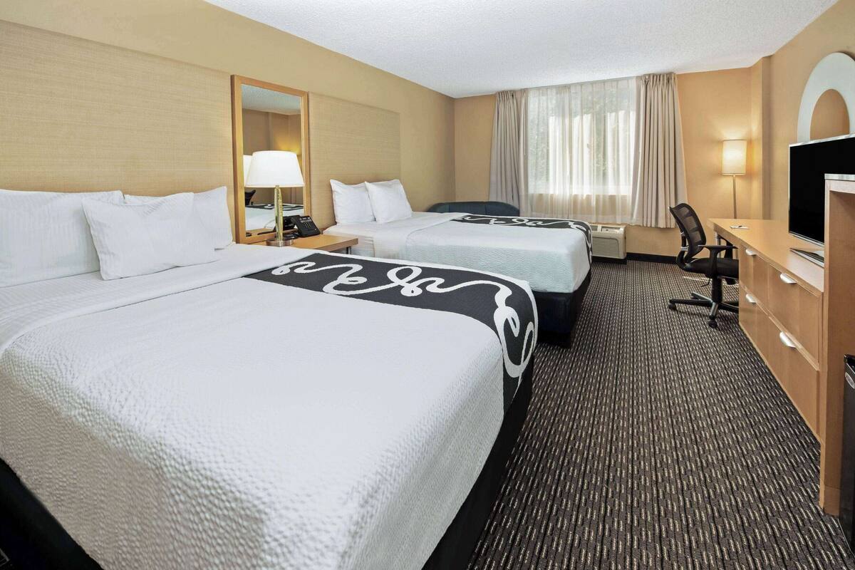 A hotel room with two beds, a desk, a chair, a TV, and a window with curtains.