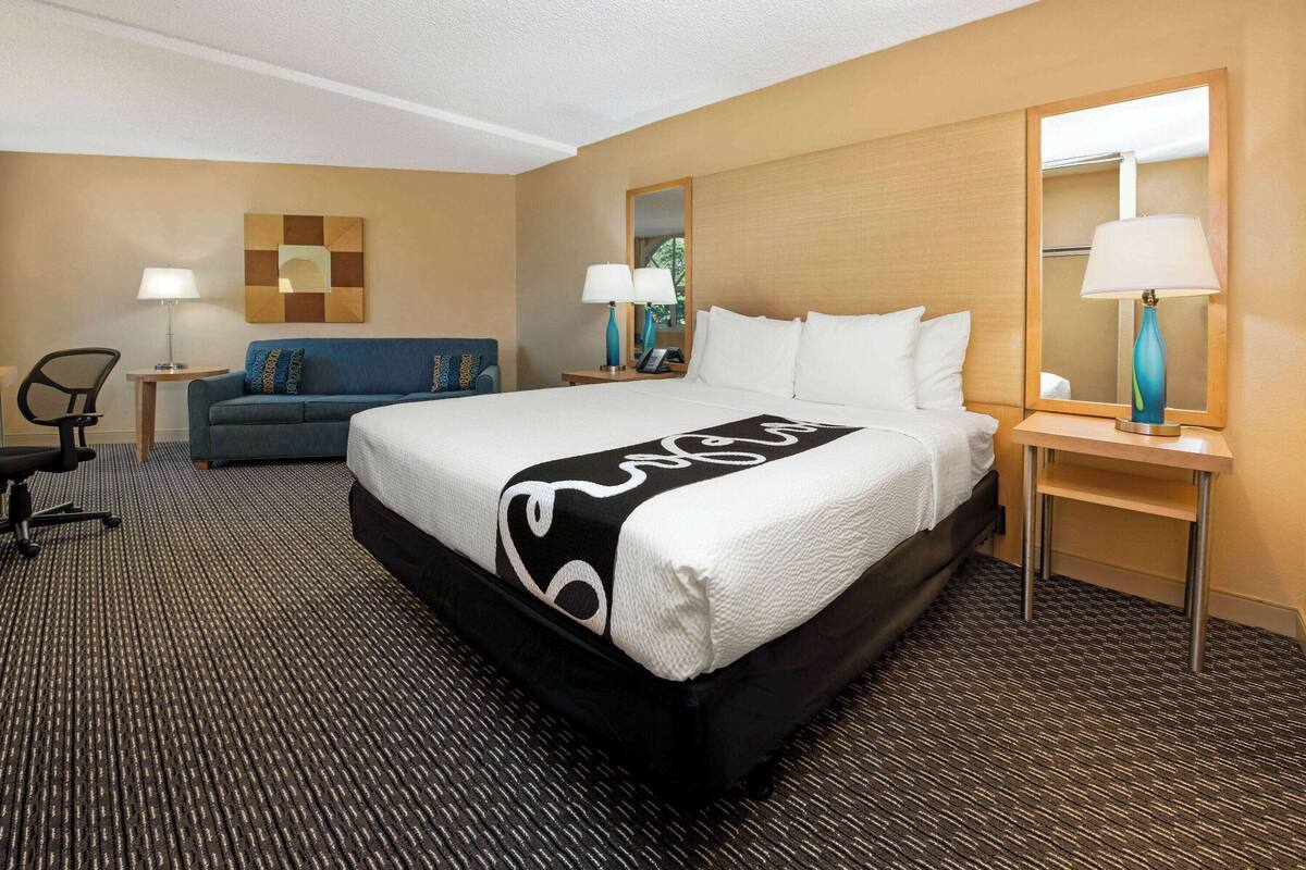 A hotel room with a large bed, a sofa, two nightstands with lamps, and a mirror.
