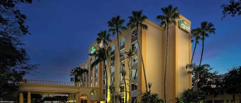 A hotel with a yellow facade, palm trees, and a covered walkway.