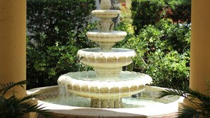 A multi-tiered fountain with water cascading down, surrounded by lush greenery and a yellow wall. - La Quinta Inn & Suites by Wyndham West Palm Beach Airport (West Palm Beach)