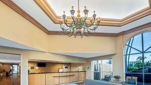 A hotel lobby with a reception desk, seating area, and a large window offering a view of the outdoors. - La Quinta Inn & Suites by Wyndham West Palm Beach Airport (West Palm Beach)