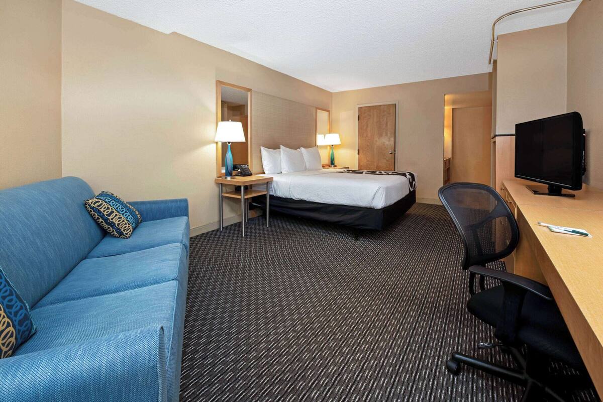 A hotel room with a bed, a desk with a computer, a chair, a sofa, and a TV.