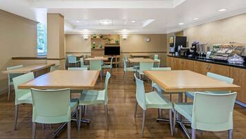 A dining area with multiple tables and chairs, a television, and a counter with food items.