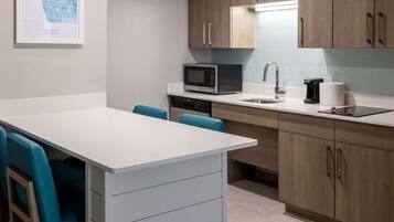 A modern kitchen with a white countertop, a microwave, a coffee maker, and wooden cabinets.