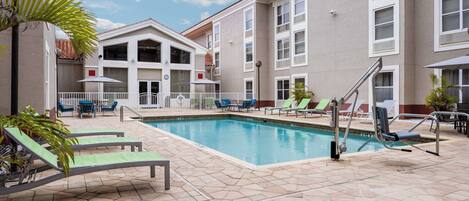 A swimming pool area with lounge chairs and a building with multiple floors and balconies.