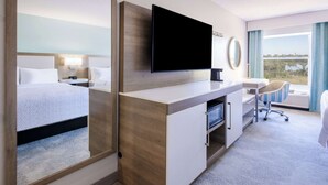 Hotellihuone, jossa on suuri sänky, työpöytä, jossa on litteänäyttöinen televisio, tuoli ja näkymä ulos.