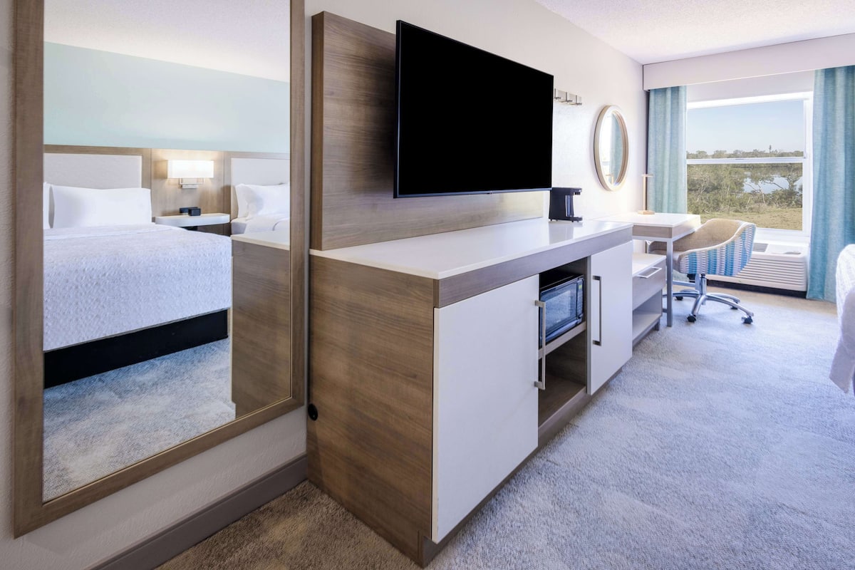 A hotel room with a large bed, a desk with a flat-screen TV, a chair, and a view of the outdoors.