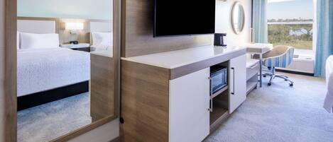 A hotel room with a large bed, a desk with a flat-screen TV, a chair, and a view of the outdoors.