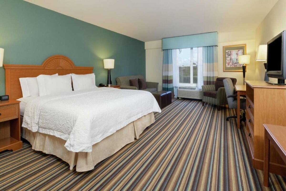 A hotel room with a large bed, a desk, a chair, a TV, and a window with curtains.