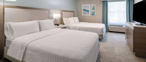 A hotel room with two beds, a desk, a TV, and a ceiling fan.