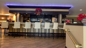 A bar area with multiple bar stools, a counter with a decorative wreath, and a ceiling with blue LED lights.