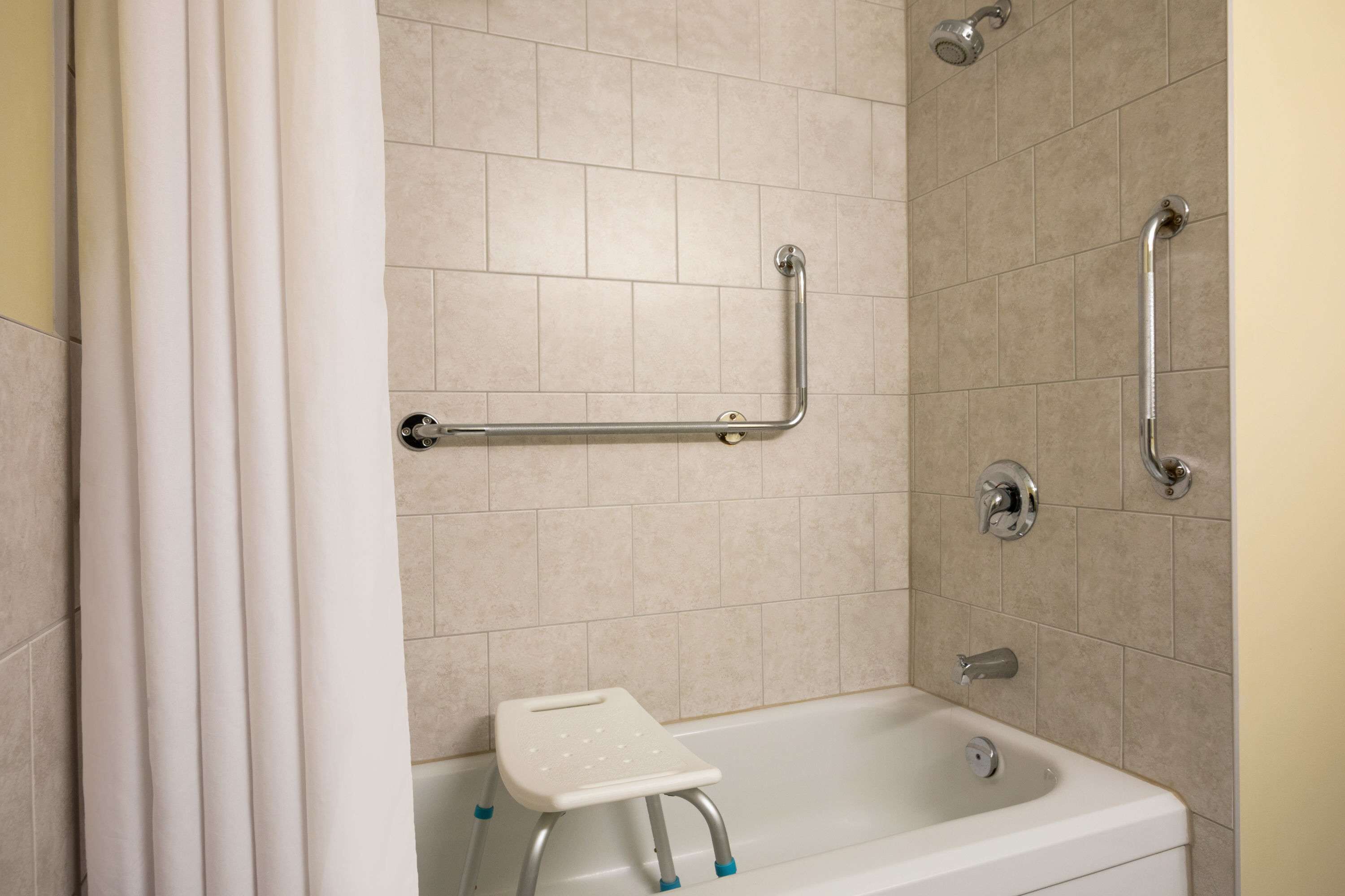A bathroom with a shower, grab bars, and a small step stool.