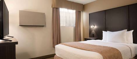 A hotel room with a large bed, a flat-screen TV, a wall-mounted air conditioner, and a window with curtains.