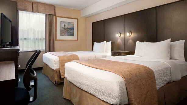 A hotel room with two beds, a desk, a TV, and a painting on the wall.