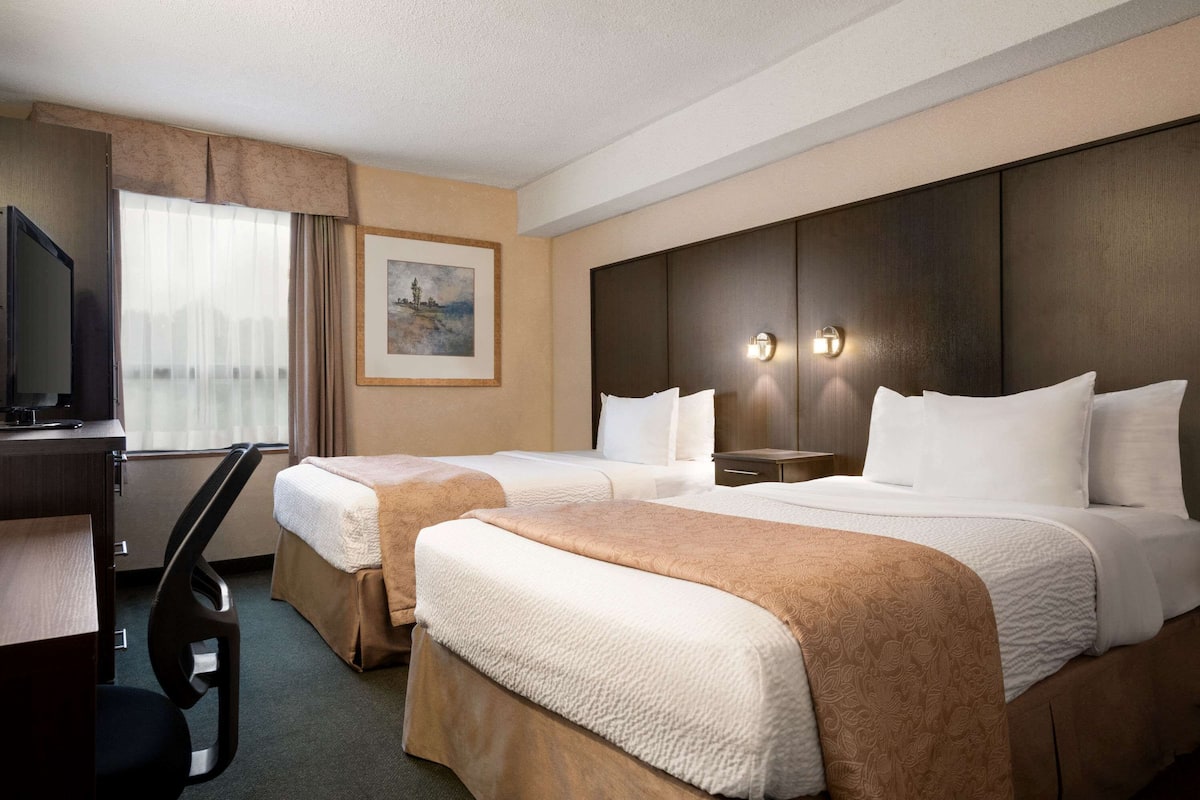A hotel room with two beds, a desk, a TV, and a painting on the wall.