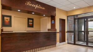 A reception area with a wooden reception desk, framed artwork on the walls, and a view through the glass doors.
