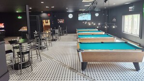 A pool hall with multiple pool tables, chairs, and a billiard rack.